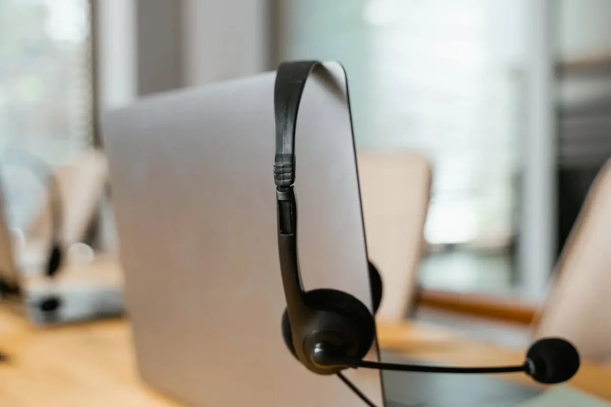 A black headset resting on a modern computer monitor in a professional office setting, symbolizing customer support and communication.