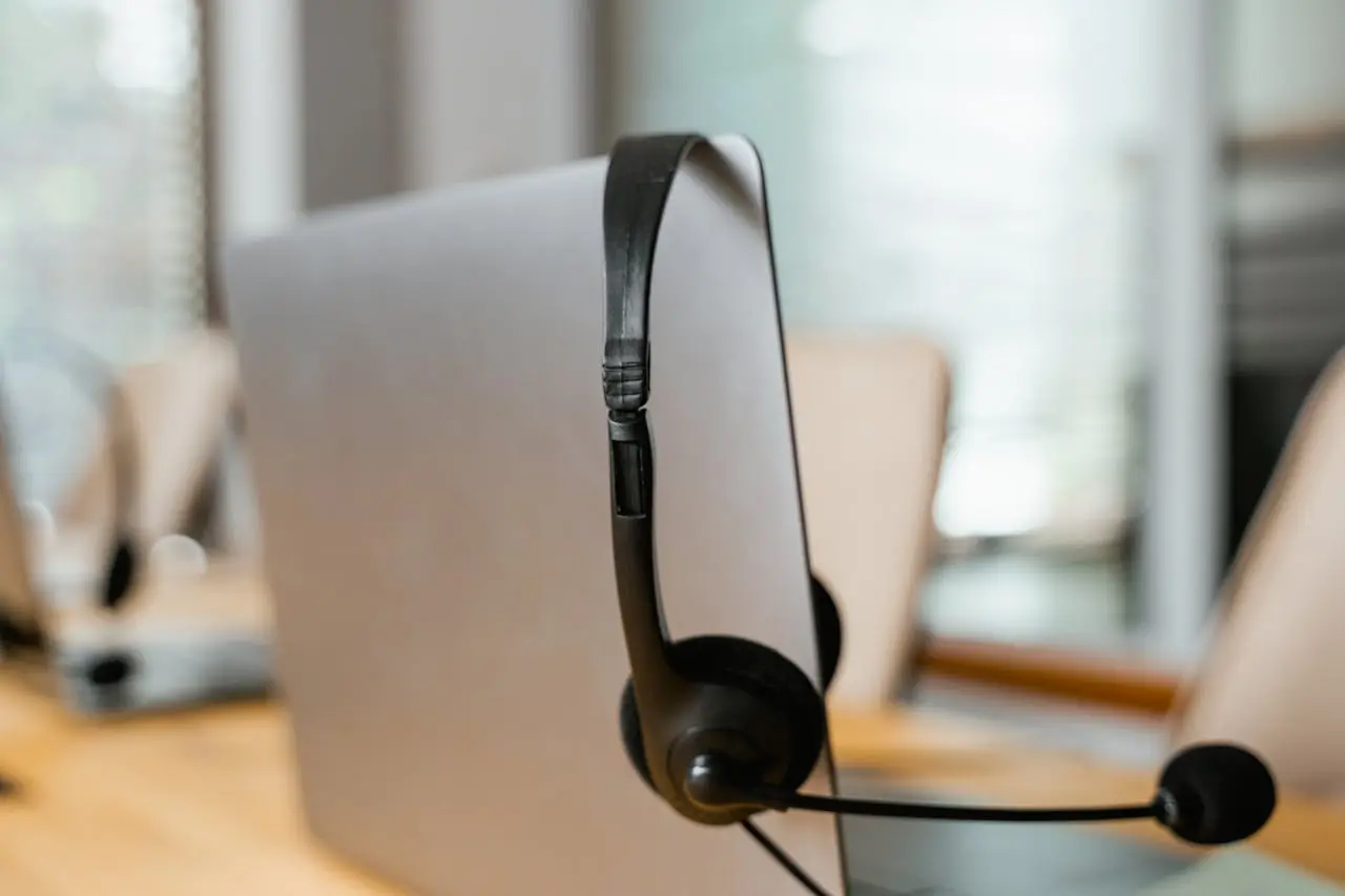 A black headset resting on a modern computer monitor in a professional office setting, symbolizing customer support and communication.