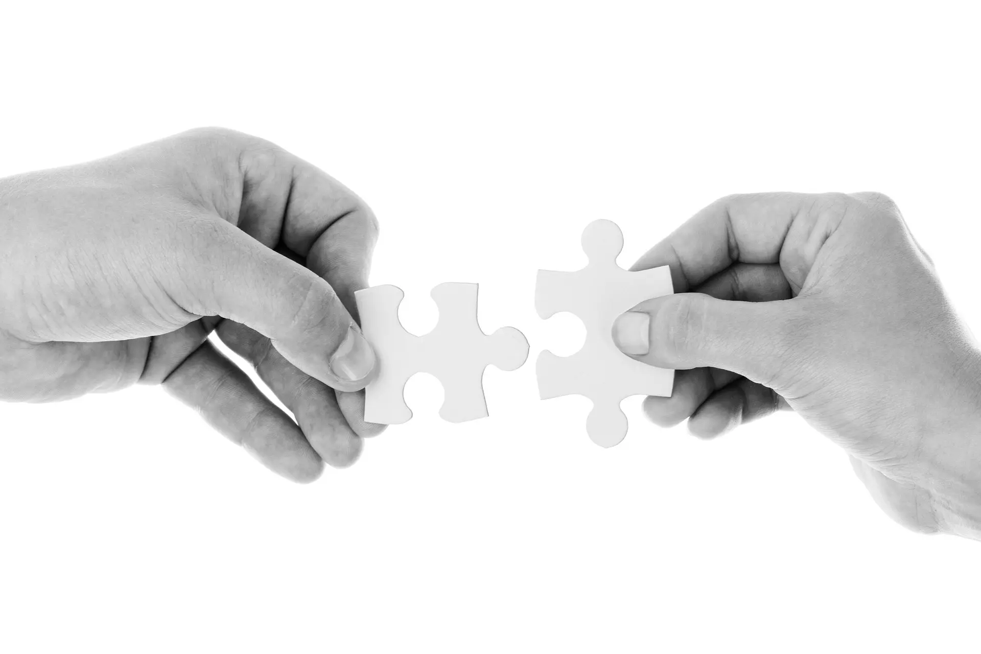 A close-up of two hands connecting white puzzle pieces, representing the process of creating a unique and custom web design solution for businesses whose needs go beyond standard pricing plans. Contact us for a tailored website