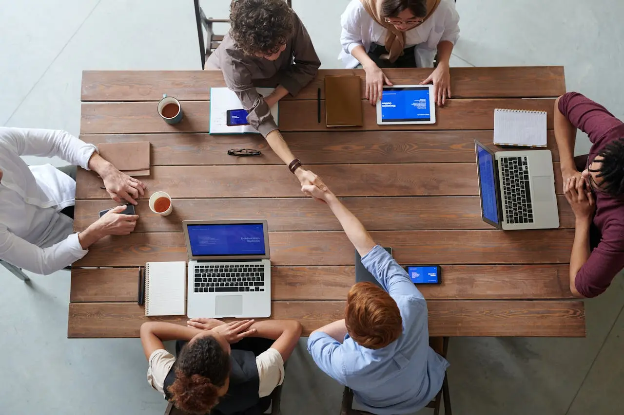 Team of professionals collaborating at a wooden table with laptops, shaking hands in agreement, representing custom websites for small businesses with affordable pricing and expert web design services.