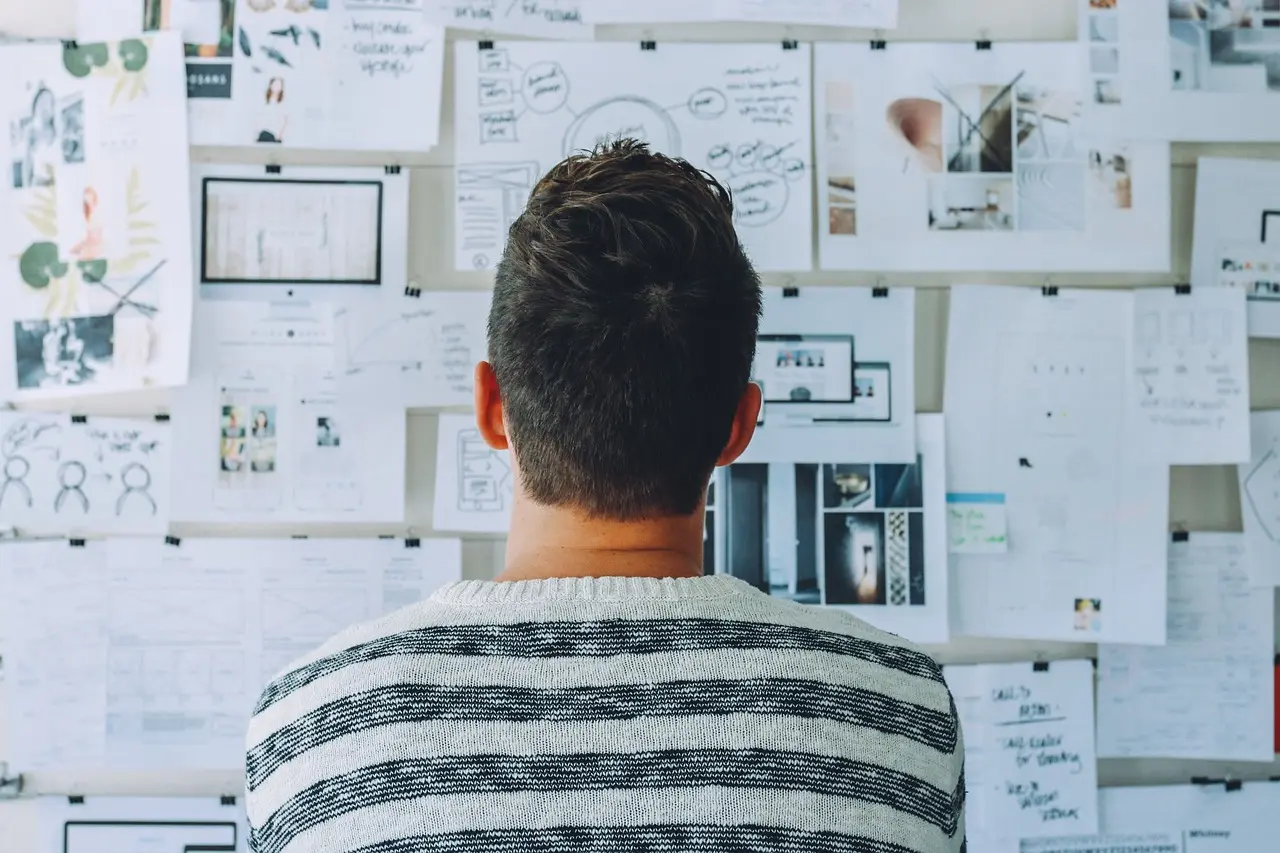 Person from behind looking at a wall covered with papers, notes, and designs, symbolizing the extensive research and ideation involved in website copywriting, as taught in Launchpad Web Designs' Copywriting Guide for Websites.