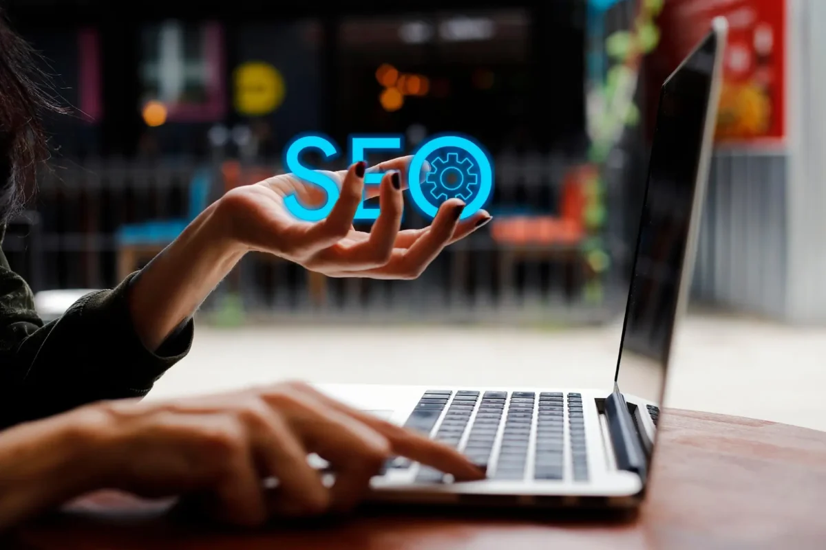 Hand holding glowing SEO text above a laptop, symbolizing Launchpad Web Designs' Local SEO Guide for Small Businesses to improve online visibility and search rankings.