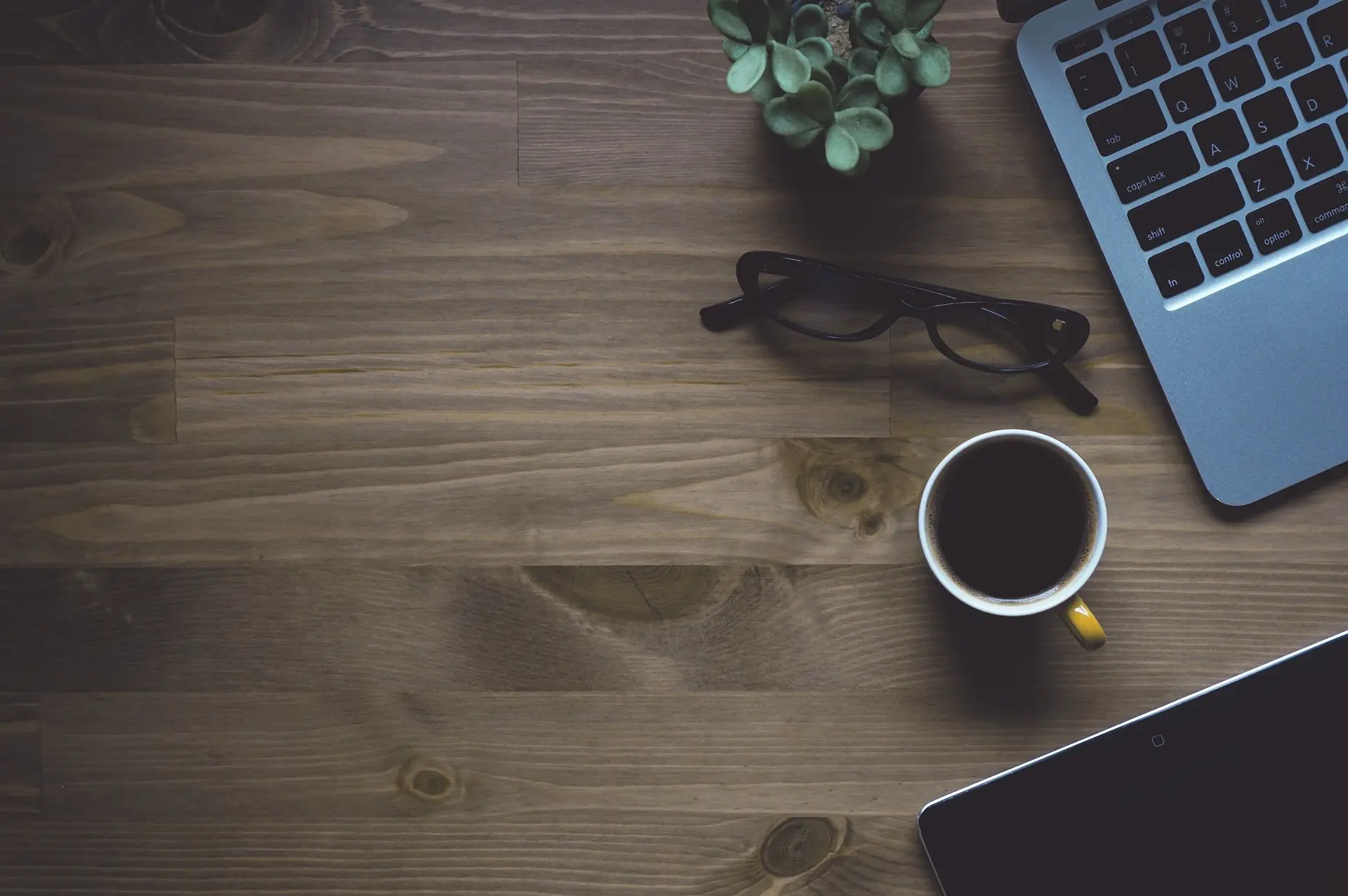 A top-down view of a professional wooden desk with a laptop, coffee, glasses, tablet, and a small plant, symbolizing the clear planning and personalized attention given to Launchpad Web Designs' custom website pricing options.