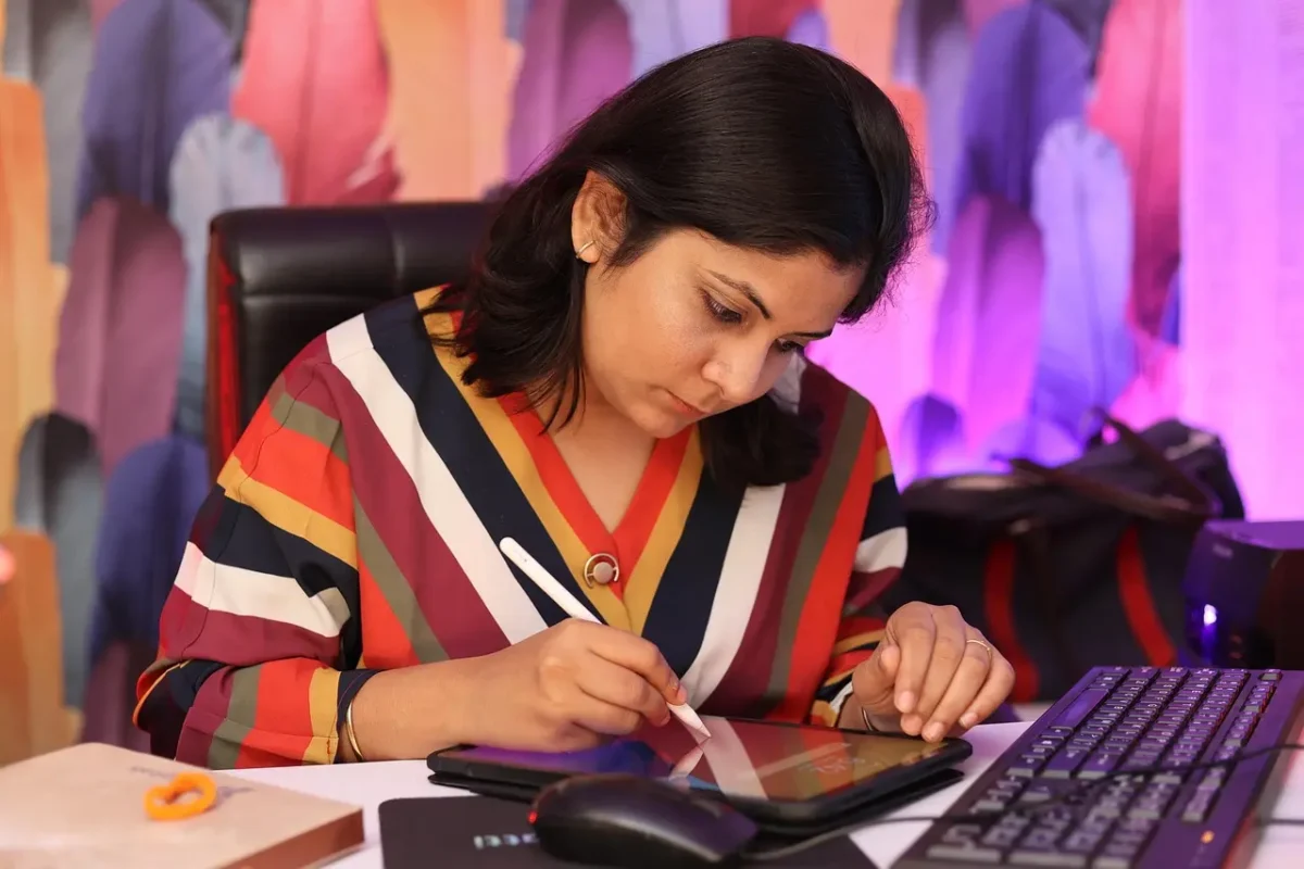 A female freelancer works at a desk, using a stylus to draw on a digital tablet while a keyboard sits next to it. This image represents website design and development services tailored for beginner freelancers and creative professionals who need a professional online presence to launch their careers.