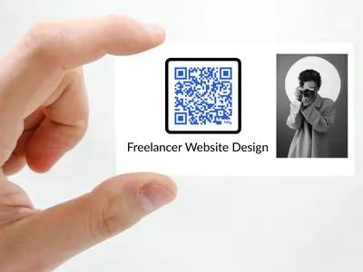 A hand holds a business card for 'Freelancer Website Design.' The card features a large QR code on the left and a black-and-white portrait of a photographer with a camera on the right, symbolizing a modern, tech-savvy approach to custom website design for freelancer marketing professionals.